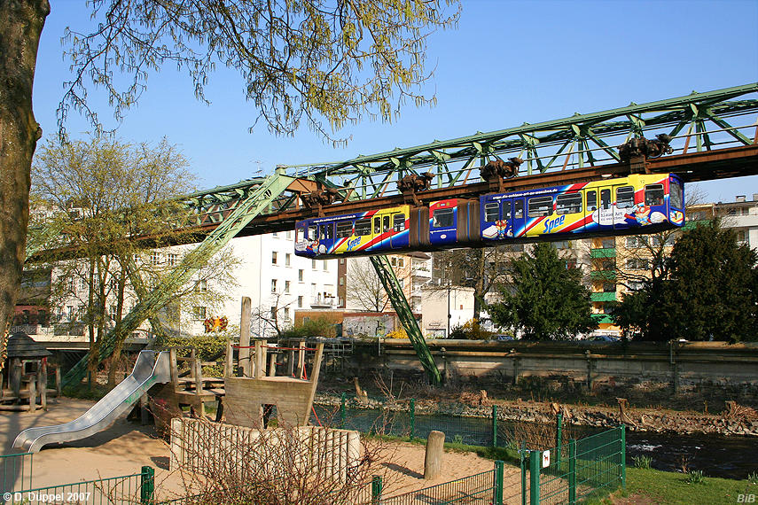 0704-40: Der mit einer farbenfrohen Vollwerbung fr ein Waschmittel versehene Wagen 12 befindet sich zischen den Stationen Wupperfeld und Obarbarmen Bf. Er passiert einen Kinderspielplatz am Wupperufer, der vormittags noch verwaist ist.